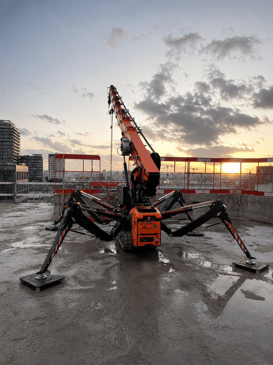 Mini-grue araignée orange déployée sur un chantier de toit au coucher du soleil.